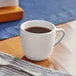 An Acopa bright white stoneware espresso cup filled with brown liquid on a table with a spoon