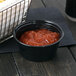 A black plastic Dart souffle cup filled with red sauce on a table.