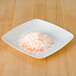 A white square plate with orange and white Rokz sugar crystals on it.