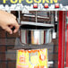 A hand holding a Carnival King 8 oz. popcorn kettle over a bag of popcorn.