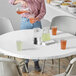 A woman pouring orange liquid into a plastic cup on a table with a Creative Converting Stay Put white tablecloth.