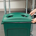 A hand putting a green Rubbermaid Slim Jim recycling container lid on a green bin with two holes.