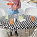 A person pouring a glass of orange liquid on a white table with a Creative Converting black and white checkered tablecloth.