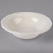 A Tuxton eggshell white scalloped edge fruit bowl on a gray surface.
