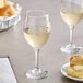 Two Acopa wine glasses filled with white wine on a table next to a plate of bread.