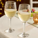 A pair of clear, stemmed wine glasses filled with white wine on a table.