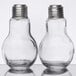 Two clear glass light bulb shaped salt and pepper shakers with metal lids on a table.
