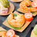 A group of Tablecraft bamboo square dishes with shrimp, tomatoes, pickles, and sandwiches on them.