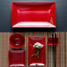 A red rectangular Elite Global Solutions sauce dish with a white border on a table with flowers and chopsticks.