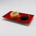 A red and black Elite Global Solutions sauce dish with food on a white plate.