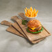 A cheeseburger and a bowl of french fries served on a rectangular faux driftwood serving board with a full pocket and handle.