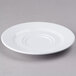 A white Elite Global Solutions double well melamine coffee saucer on a gray surface.