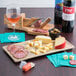 A GET faux oak wood melamine charcuterie serving board on a table with a cheese and meat platter and a glass of wine.