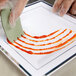 A gloved hand using a Mercer Culinary silicone plating tool to paint a design on a plate.