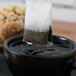 A Bromley Organic Green Tea bag being poured into a black cup of liquid.