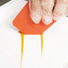 A person using a Mercer Culinary silicone wedge plating tool to place an orange wedge on a white plate.