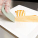 A person in gloves using a Mercer Culinary square notch plating tool to cut a white object.