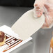 A hand using a white Mercer Culinary silicone wedge plating tool to plate a dessert.