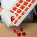 A gloved hand holding a tray of red heart-shaped jelly molds.