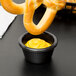A Carlisle black fluted melamine ramekin filled with yellow mustard on a table with pretzels.