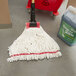 A Rubbermaid wet mop with a white looped end on the floor next to a bucket.