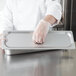 A person wearing gloves holding a Choice stainless steel steam table pan cover over a tray.