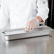 A chef wearing gloves and holding a Choice stainless steel slotted steam table pan cover.