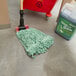 A green Rubbermaid Super Stitch wet mop head on the floor.