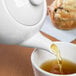 A white Libbey Royal Rideau teapot pouring tea into a white tea cup with a muffin on the side.