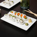 A rectangular white porcelain tray with sushi rolls on a table.