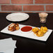 A Libbey rectangular porcelain tray with 3 plates of food and sauce on a table.