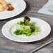A Libbey white wide rim porcelain plate with a green salad on it on a table.