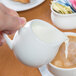A person using a Libbey Royal Rideau white pitcher to pour milk into a cup of coffee.
