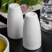 Two white Libbey Royal Rideau porcelain pepper shakers on a table.