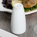 A white Libbey Royal Rideau porcelain pepper shaker next to a plate of food.