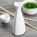 A white porcelain Libbey Sake bottle on a table with a bowl of seaweed and chopsticks.
