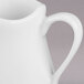 A close-up of a white Libbey Royal Rideau porcelain creamer with a handle.