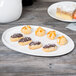 A Libbey white porcelain platter with chocolate covered pastries on a table.