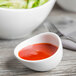 A close up of a Libbey Royal Rideau white porcelain sauce bowl filled with red sauce on a white surface.