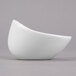 A close up of a Libbey Royal Rideau white porcelain sauce bowl with a curved edge on a gray surface.