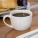 A close-up of a Libbey Royal Rideau white low espresso cup full of coffee on a table next to a plate of bread.