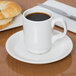 A white Libbey Stacking Porcelain mug filled with brown liquid on a saucer with a croissant.