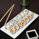 A rectangular white porcelain tray with a sushi roll and chopsticks on it.