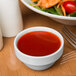 A white Libbey stacking ramekin filled with red sauce next to a plate of salad.