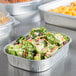 Durable Packaging silver mini foil pan with broccoli and carrot salad on a table.