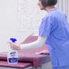 A woman in blue scrubs using Purell Healthcare Surface Disinfectant to clean a surface.