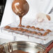 A chef pouring chocolate into a Matfer Bourgeat chocolate mold tray.