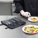 A person in a kitchen wearing gloves uses Mercer Culinary Precision Plating Tongs to prepare a meal.
