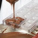 A person using a Chocolate World wickerwork square plastic mold to pour chocolate.