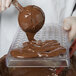 A person pouring chocolate into a Matfer Bourgeat coffee bean chocolate mold.